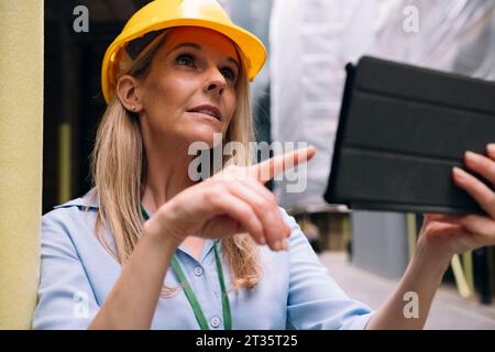 Engineer pointing at tablet PC leaning on pole Stock Photo