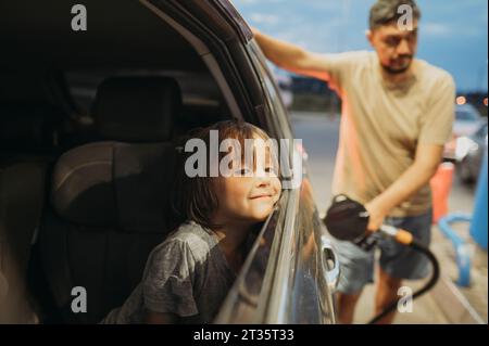 Son sitting with father refueling car at station Stock Photo