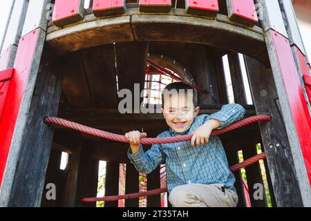 Smiling boy sitting on outdoor play equipment in playground Stock Photo