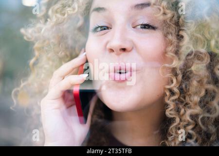 Smiling young woman with curly hair talking on phone Stock Photo