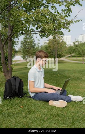 Boy using laptop sitting on grass at park Stock Photo