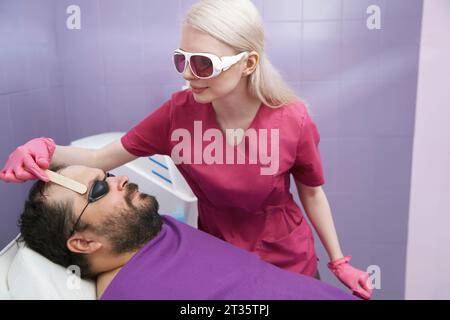 Dermatologist doing hair removal treatment of client at clinic Stock Photo