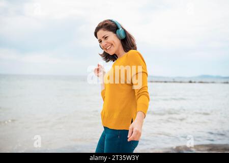 Happy woman wearing wireless headphones dancing at beach Stock Photo