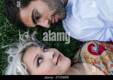 Romantic couple staring at each other lying on grass Stock Photo