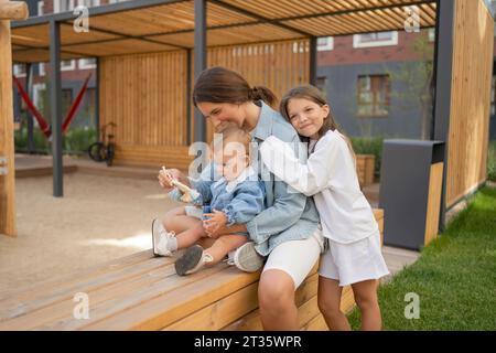 Mother with children spending leisure time on bench in back yard Stock Photo