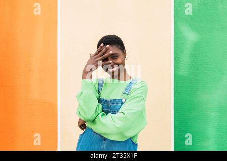 Happy young woman touching forehead standing in front of multi colored wall Stock Photo