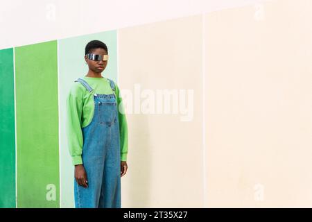 Young woman wearing smart glasses standing in front of multi colored wall Stock Photo