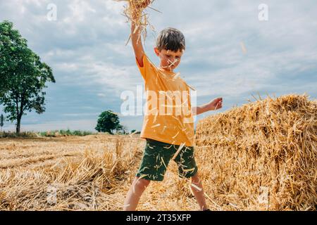 Boy playing with hay in wheat field on sunny day Stock Photo