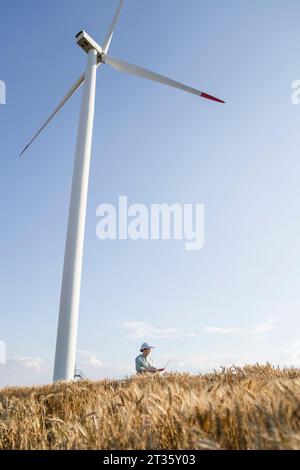 Agronomist standing under wind turbine on sunny day Stock Photo