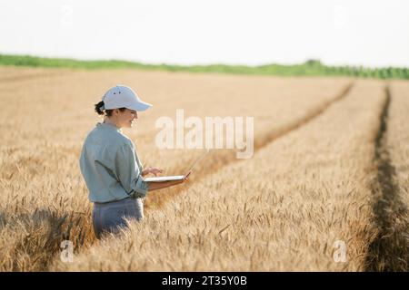 Smiling farmer using laptop in field on sunny day Stock Photo