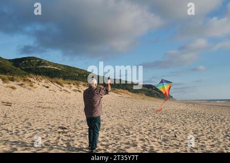 Senior man flying kite under cloudy sky on sunny day at beach Stock Photo