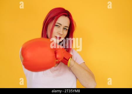 Woman wearing boxing gloves against yellow background Stock Photo