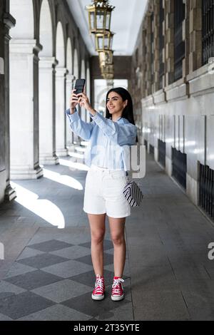 Young woman taking selfie with smart phone in colonnade Stock Photo