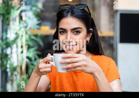 Smiling young woman enjoying coffee at cafe Stock Photo