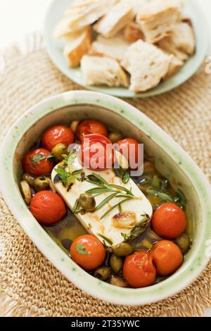 Baked feta cheese with olives, cherry tomatoes and herbs Stock Photo