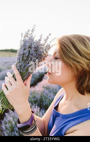 Woman with eyes closed smelling bunch of lavender flowers in field Stock Photo