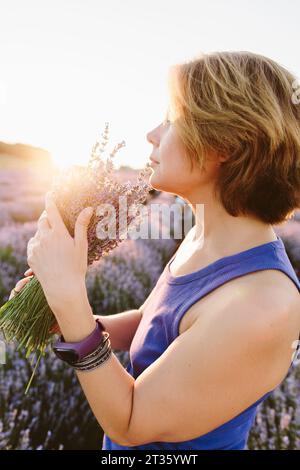 Woman smelling bunch of lavender flowers in field Stock Photo