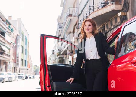 Happy businesswoman getting out of red car on street Stock Photo