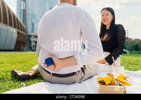 Man hiding jewelry box behind back in front of happy woman Stock Photo