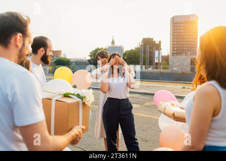 Friends surprising woman with balloons and gift box at sunset Stock Photo