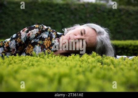 Senior woman lying on plants in park Stock Photo