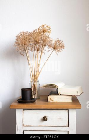 Books, mug and dried Allium flowers on small cabinet Stock Photo