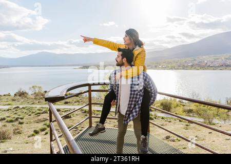 Man giving piggyback ride to girlfriend pointing at observation point Stock Photo
