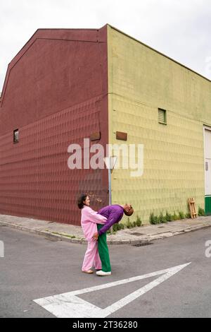 Woman holding friend bending backwards in front of building Stock Photo