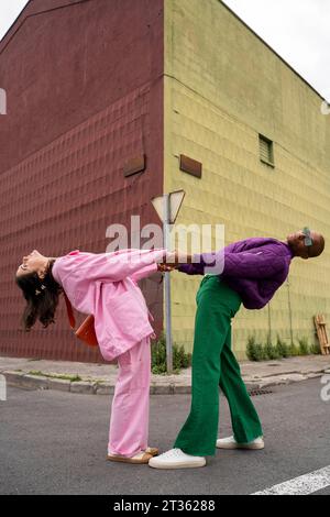 Friends holding hands and bending together in front of building Stock Photo