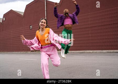 Cheerful woman dancing with friend jumping in front of building Stock Photo