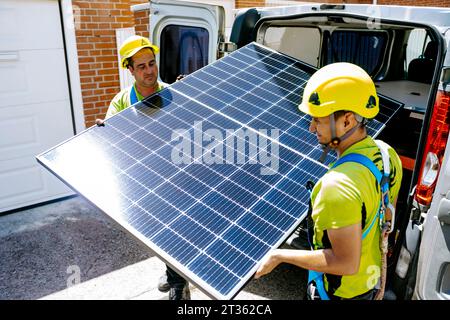Engineers wearing hardhat carrying solar panel on sunny day Stock Photo