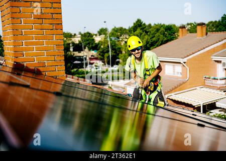 Happy engineer with drill machine installing solar panels on roof Stock Photo