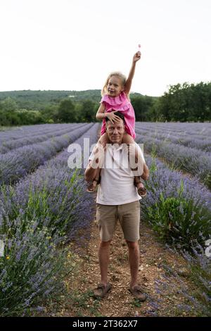 Happy daughter with arm raised sitting on father's shoulders Stock Photo