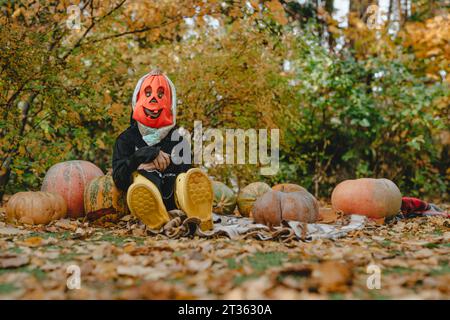 Playful girl in halloween costume sitting amidst pumpkins in garden Stock Photo