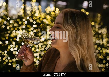 Happy woman holding champagne glass near Christmas lights Stock Photo