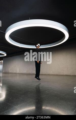 Young woman using VR glasses and jumping in parking garage Stock Photo