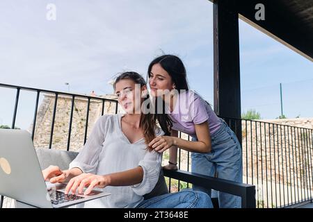 Two young women using laptop on balcony Stock Photo