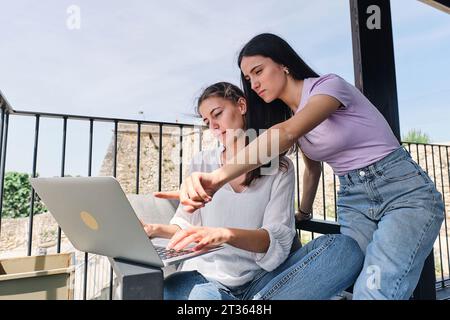Two young women using laptop on balcony Stock Photo