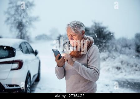 Senior man using smart phone near car in snow Stock Photo