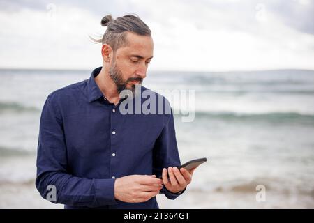 Mature man using smart phone at beach Stock Photo