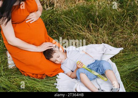 Pregnant mother stroking sleeping son on grass Stock Photo