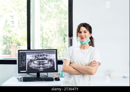 Smiling dentist with arms crossed standing near x-ray Image on computer screen Stock Photo