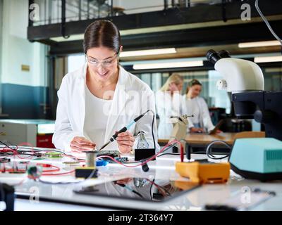 Happy engineer examining and measuring circuit board with multimeter Stock Photo