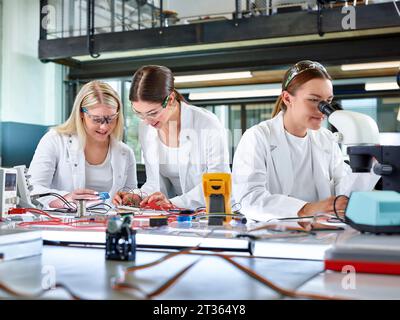 Young engineers measuring with multimeter and colleague examining through microscope Stock Photo