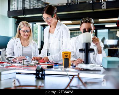 Engineer teaching trainee with colleague looking through microscope Stock Photo