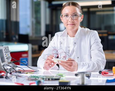Smiling young scientist sitting with circuit board in laboratory Stock Photo