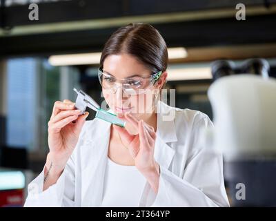 Smiling young trainee measuring circuit board with caliper in laboratory Stock Photo