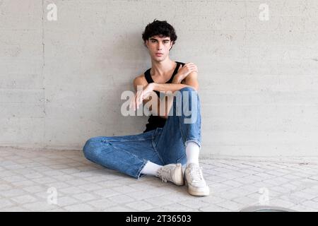 Young man sitting in front of wall Stock Photo