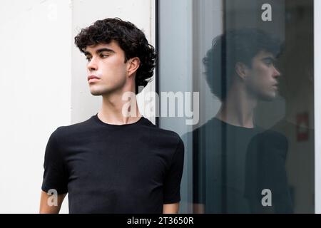 Thoughtful young man standing near glass window Stock Photo