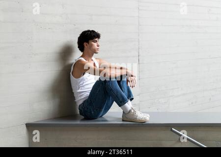Thoughtful young man sitting on wall Stock Photo